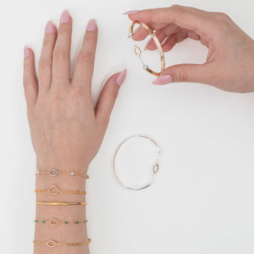 A person's hands showcasing an assortment of gold-colored wire bracelets in various designs, with one hand holding a single bracelet while the other displays multiple bracelets on the wrist.