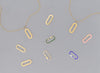 A collection of flat paper clip-shaped invisible clasps in various colors including gold, silver, green, pink, and blue, displayed on a grey background.