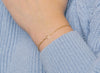 A gold heart-shaped wire charm connector worn as a bracelet on a person's wrist, with a sweater in the background.