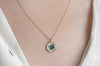 Gold necklace with a circular pendant featuring blueberries on a person wearing a white top.
