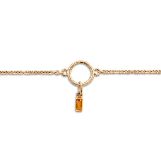 Gold necklace with a small yellow gemstone pendant on a white background.