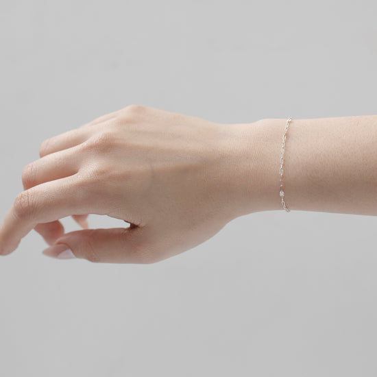 Hand wearing a delicate bracelet on a plain background