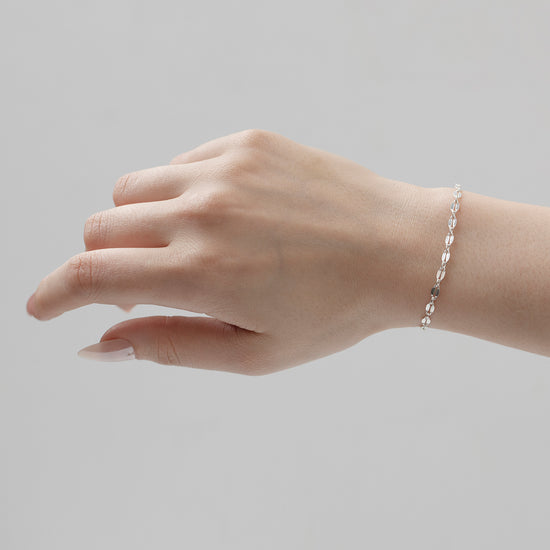 A person's hand wearing a silver hammered cable chain bracelet.