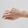Hand wearing a delicate silver bracelet on a plain background