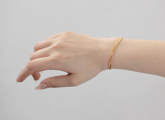 Hand wearing a gold bracelet on a plain background