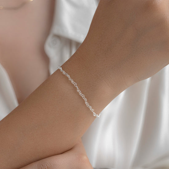 Silver heart stylized bracelet on a person's wrist with a white shirt background