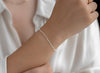 Silver heart stylized bracelet on a person's wrist with a white shirt background