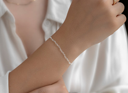 Silver heart stylized bracelet on a person's wrist with a white shirt background