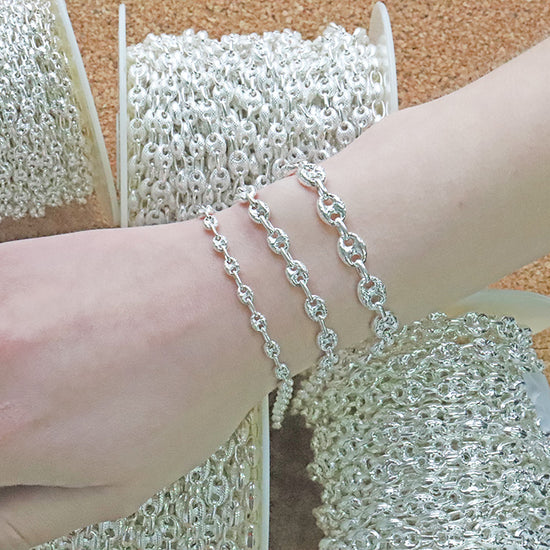 Silver mariner chain bracelet on a wrist with spools of chain in the background