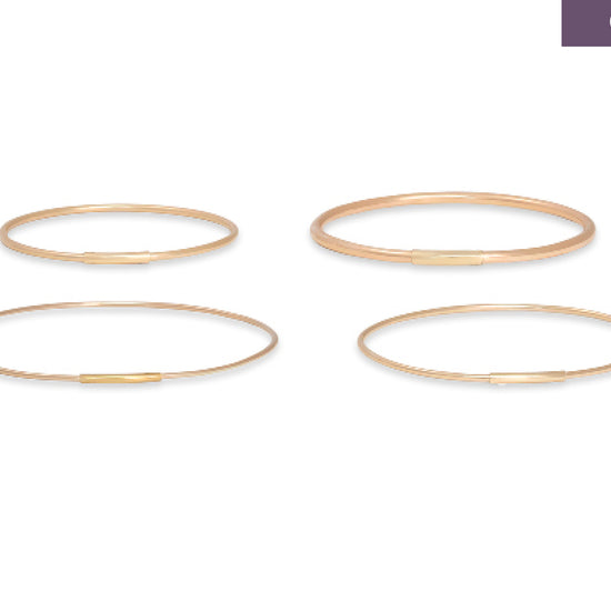Four gold oval permanent bangles on a white background