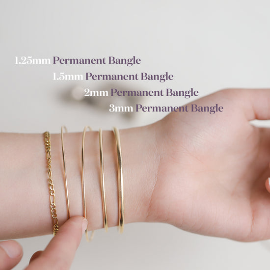Hand wearing multiple gold bangles with size labels on a light background