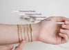Hand wearing multiple gold bangles with size labels on a light background