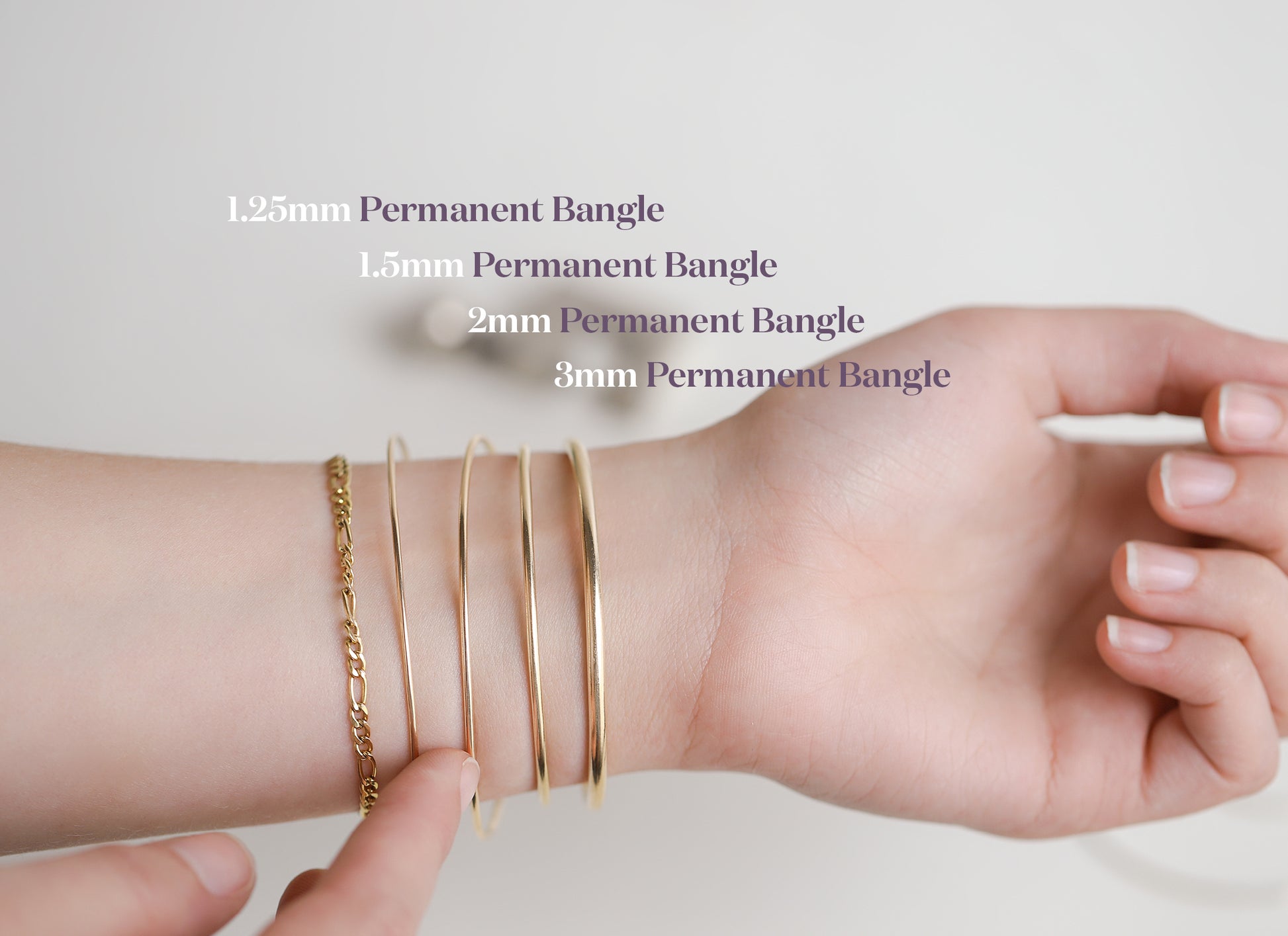 Hand wearing multiple gold bangles with size labels on a light background