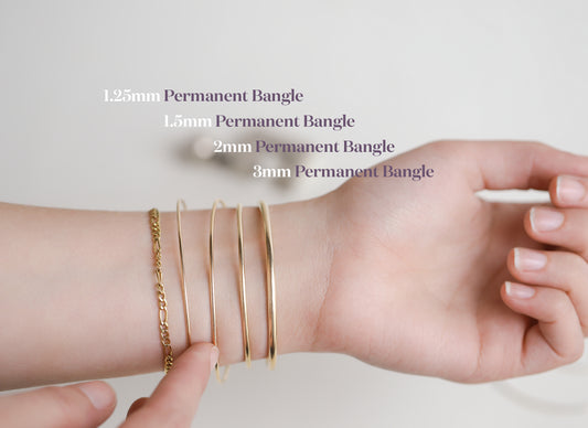 Hand wearing multiple gold bangles with size labels on a light background