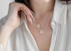 Necklace with circular pendants worn by a person in a white shirt.