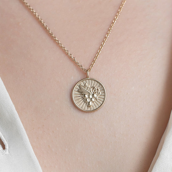 Gold necklace with a round pendant on a person wearing a white blouse.