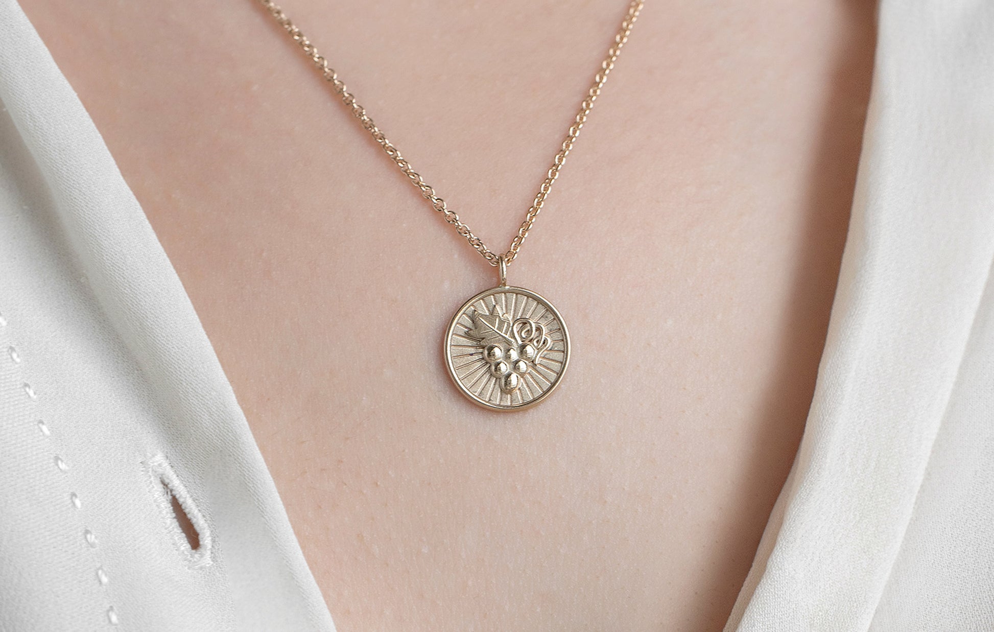 Gold necklace with a round pendant on a person wearing a white blouse.