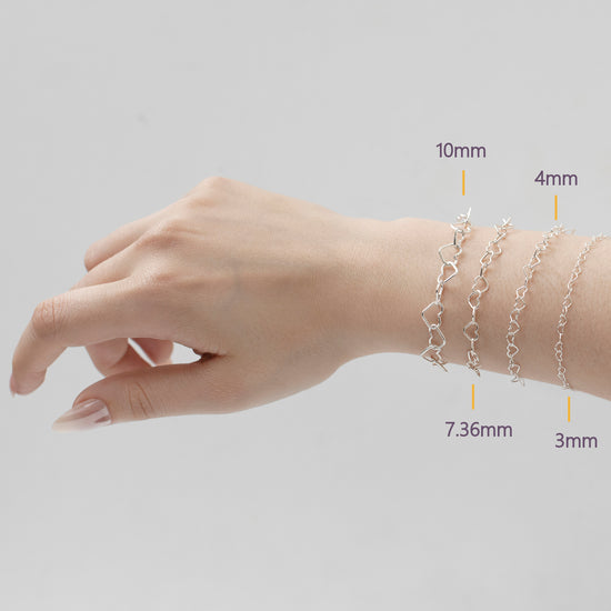 Hand wearing four silver heart bracelets with measurements indicated on a light gray background