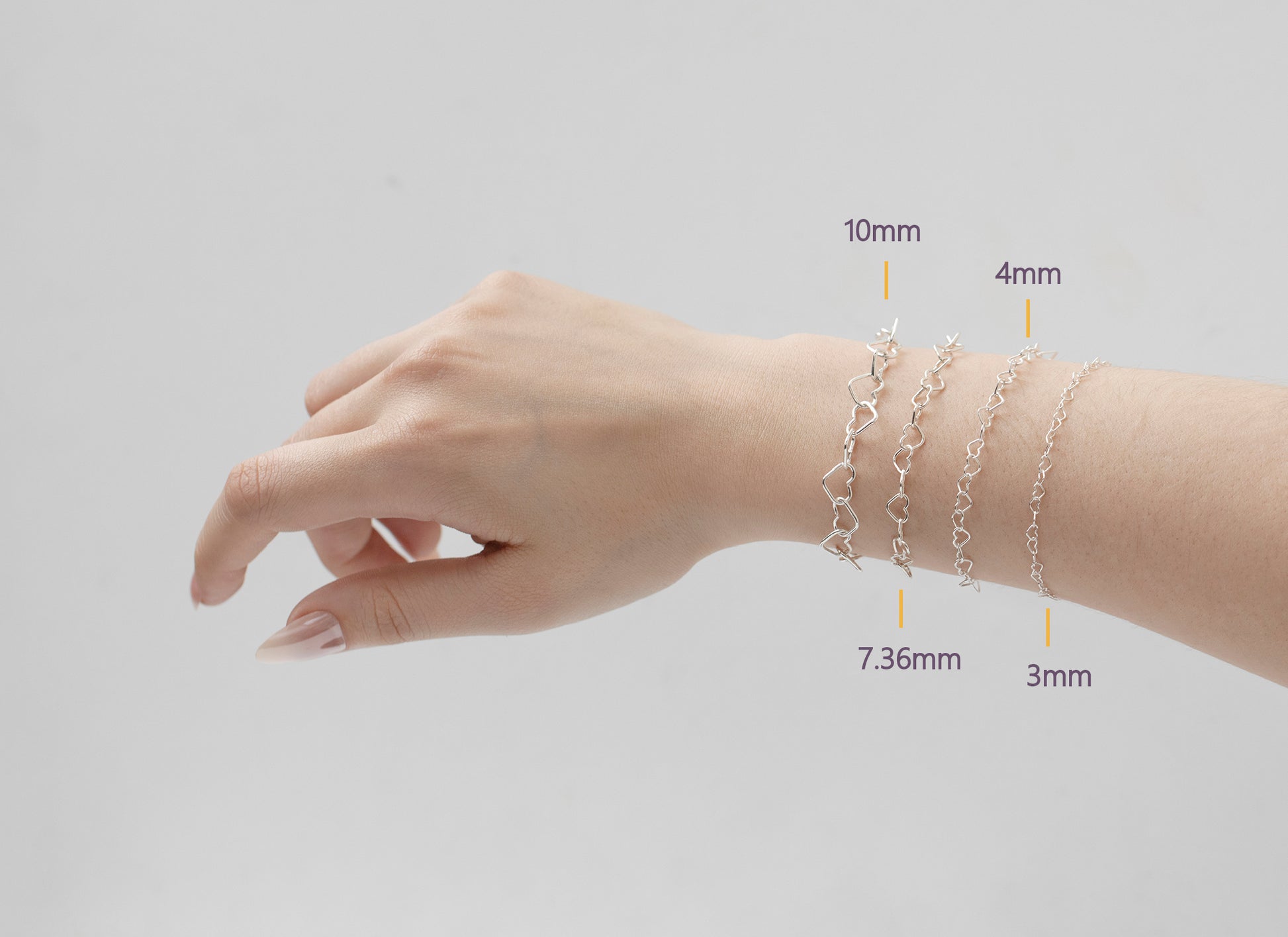 Hand wearing four silver heart bracelets with measurements indicated on a light gray background