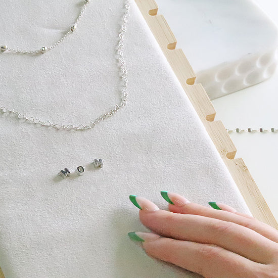 Silver jewelry on a white surface with a hand touching it