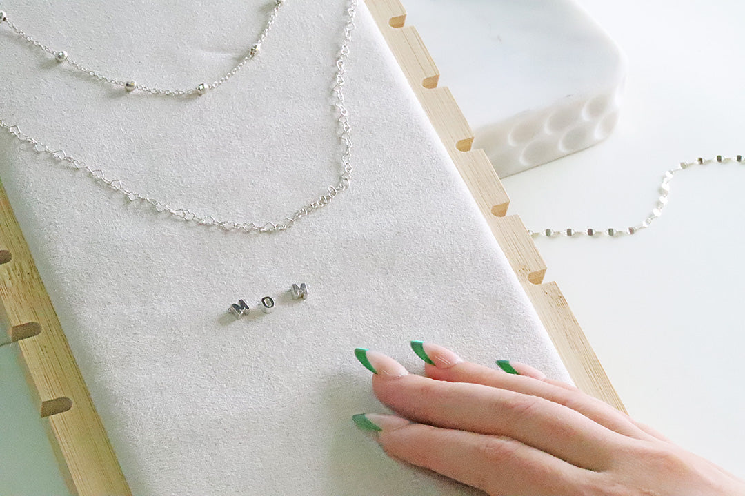 Silver jewelry on a white surface with a hand touching it