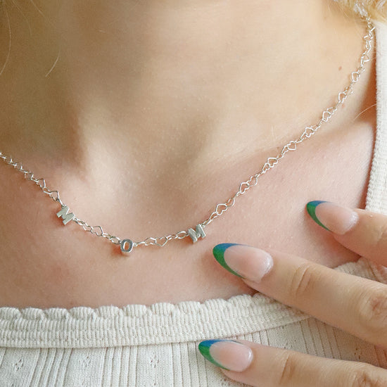 Silver necklace being worn on a person's neck with a close-up of the necklace.