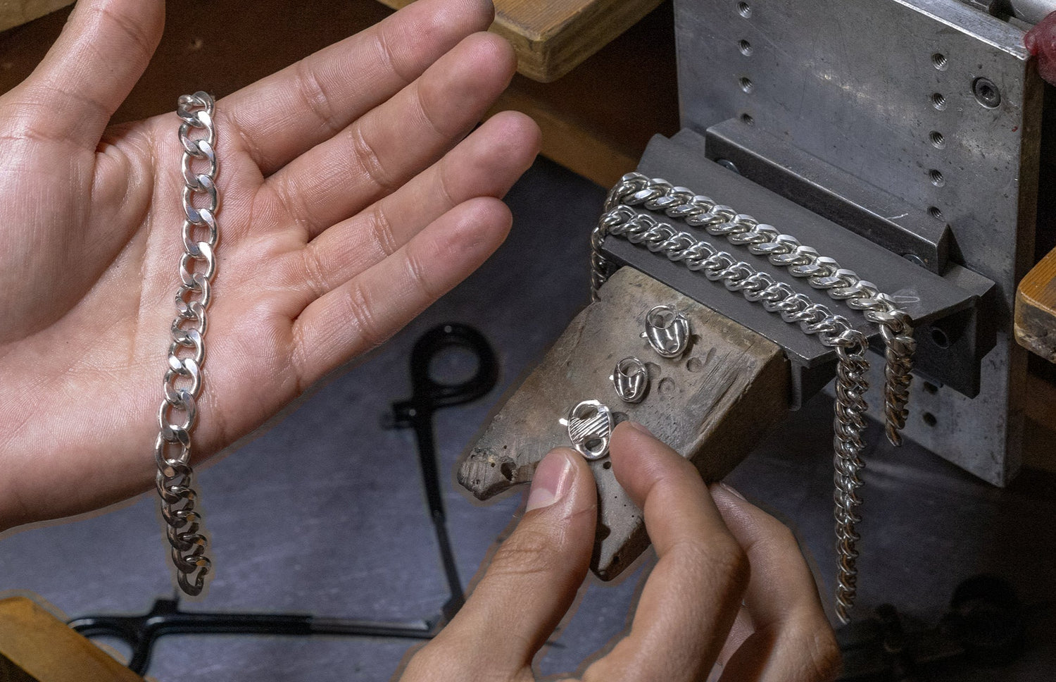 Person holding a silver chain next to a metal chain-making tool.