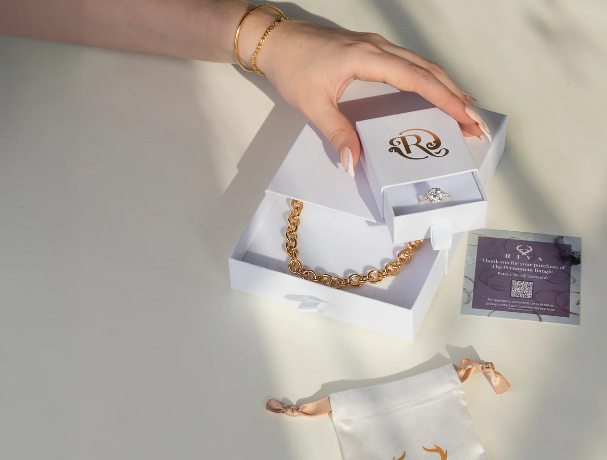 Jewelry set with gold chain, earrings, and card in a box on a light background