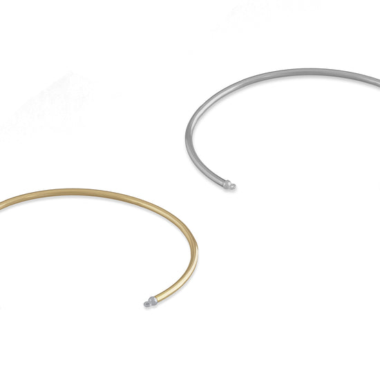 Two round wire permanent cuffs, one in gold color and the other in silver color, both with bails on the caps for attaching charms.