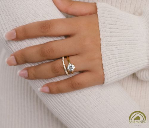 Hand model wears Round Diamond Solitaire Engagement Ring Mounting in Fairmined Yellow Gold with half-pave wedding band, from RIVA Precision