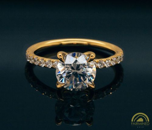 A round diamond pavé engagement ring semi-mount in Fairmined yellow gold, featuring melee diamonds on the shank and a comfort fit inner curve.