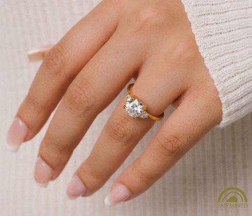 Hand model wearing Round Diamond Three-Stone Engagement Ring Semi-Mount in Fairmined Yellow Gold from RIVA Precision