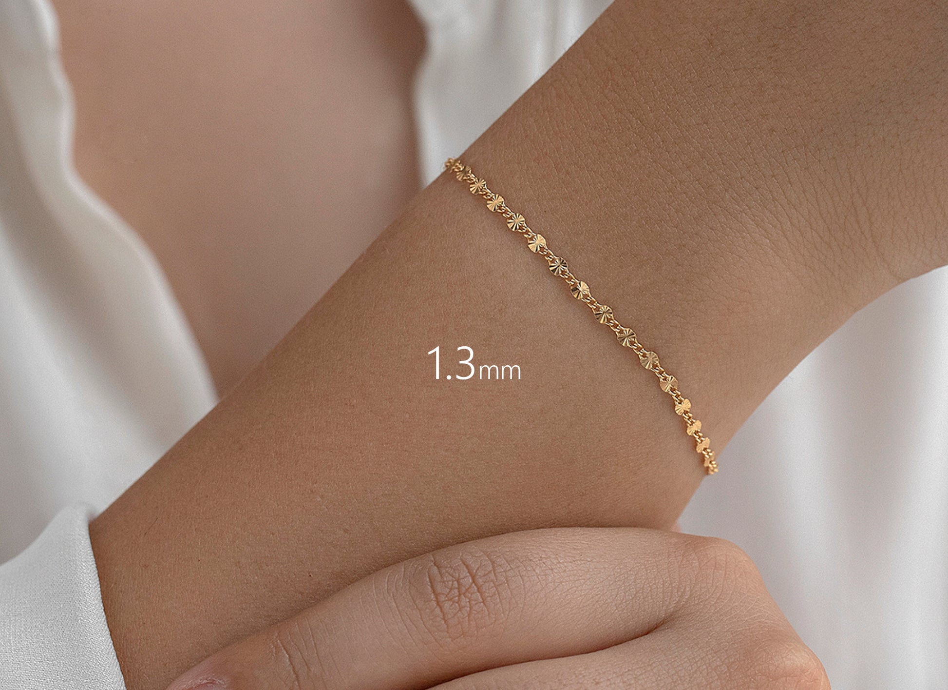 Gold bracelet on a wrist with a measurement label '1.3 mm' against a white background