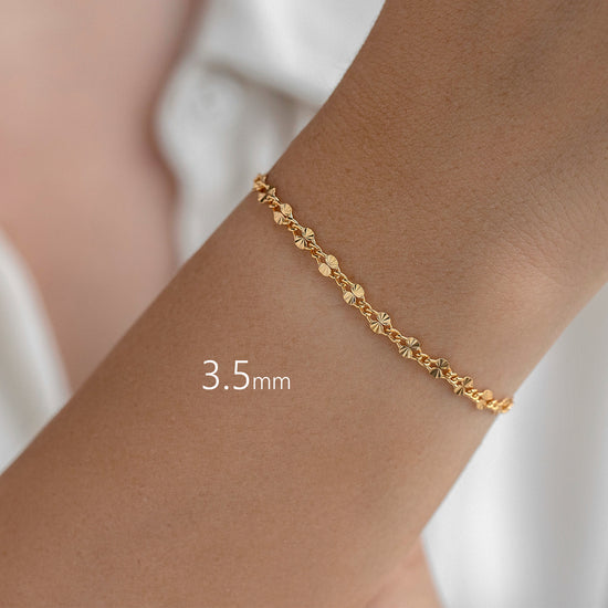 Gold starburst link bracelet on a wrist with a plain background